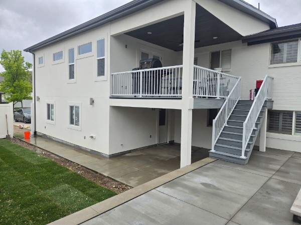 White two-story house with a covered upper deck, exterior stairs and concrete patio.